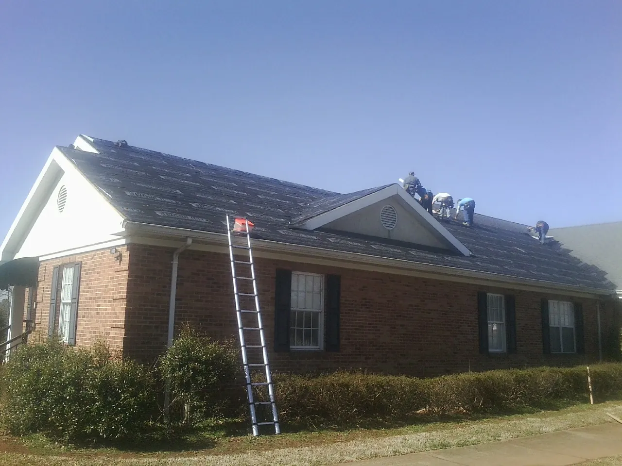 Crew tearing shingles off a brick ranch roof with a ladder set — Metal Roof Repair work by our crew in Kulpmont