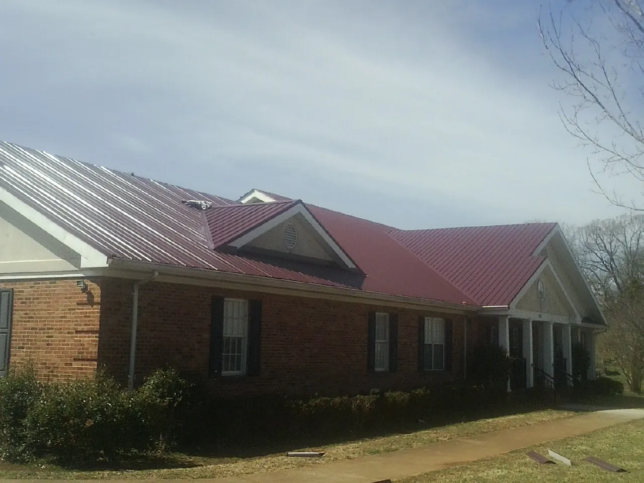 Red metal roof with gabled entries on a long brick building, from a Hail Damage Roof Repair job in Kulpmont