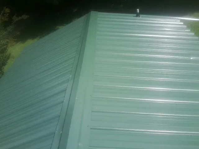 New green metal panels meeting at the ridge of a roof — Flat Roof Repair work by our crew in Kulpmont