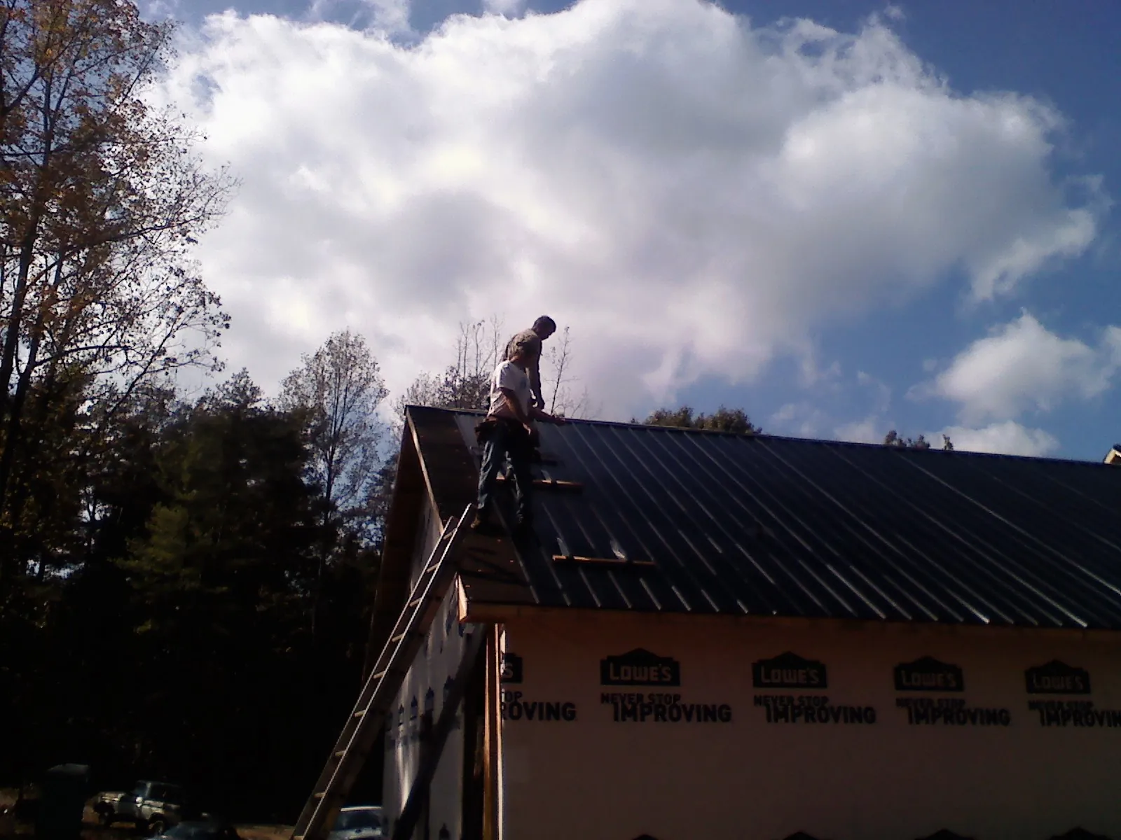 Roofer fastening dark metal panels high against a cloudy sky, from a Roof Inspection job in Kulpmont