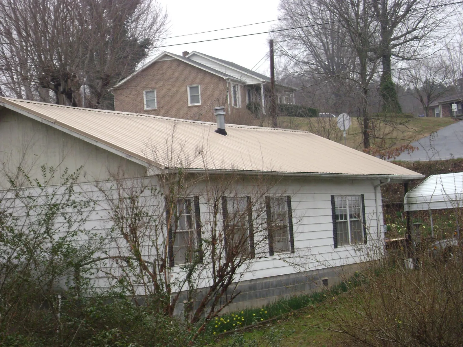 Tan metal roof on a white sided house set into a hillside — Commercial Roofing by Roofing Brothers in Kulpmont